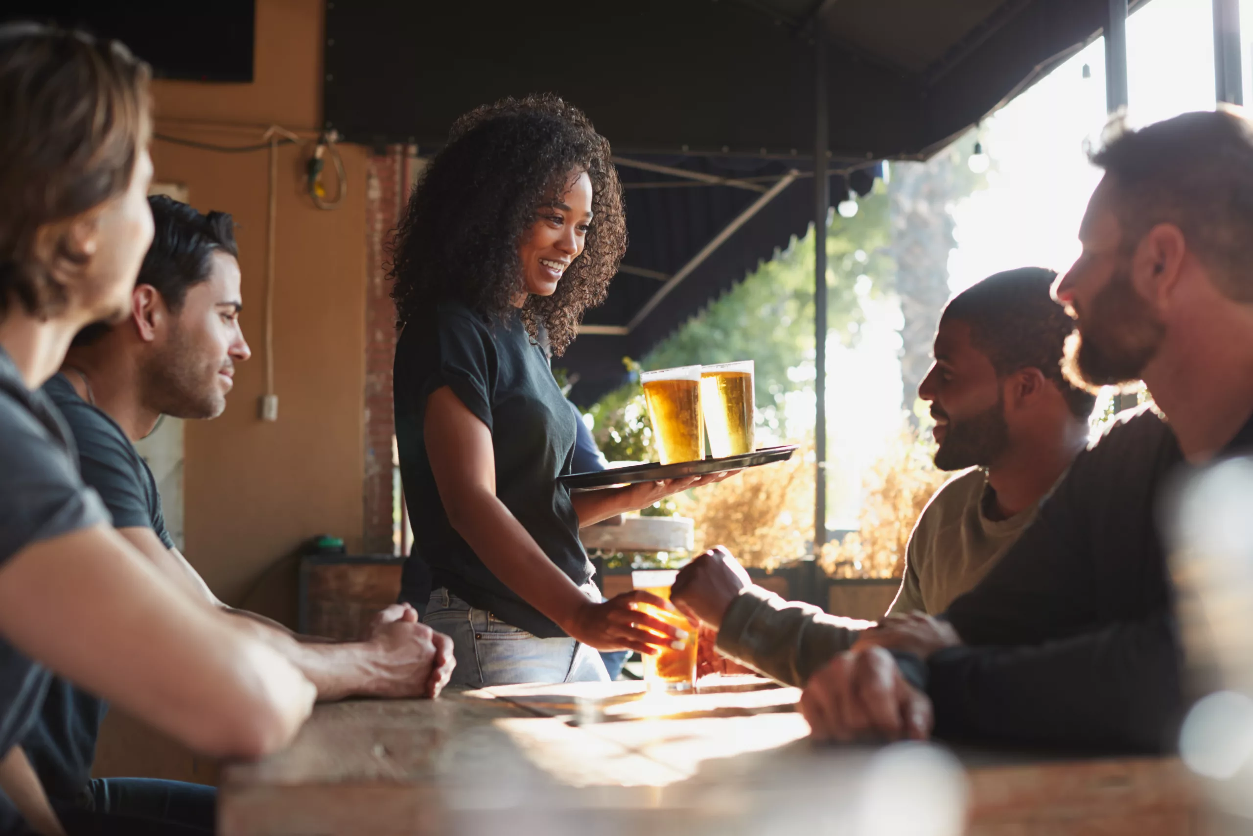 Serveuse qui donne des verres de bière à une table de clients qui sourient